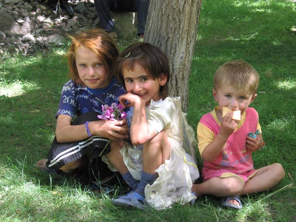 three children sit under a tree in Tajikistan