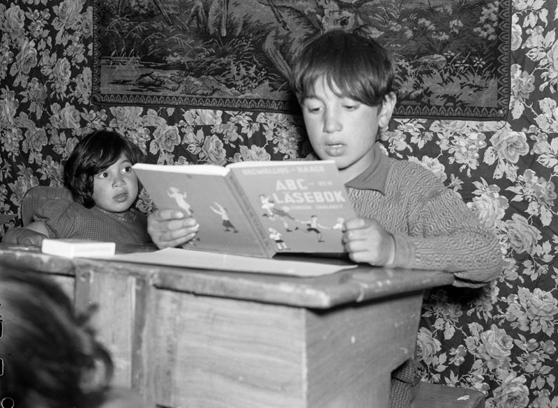 a black and white photo of a young boy reading a book while a younger child looks on